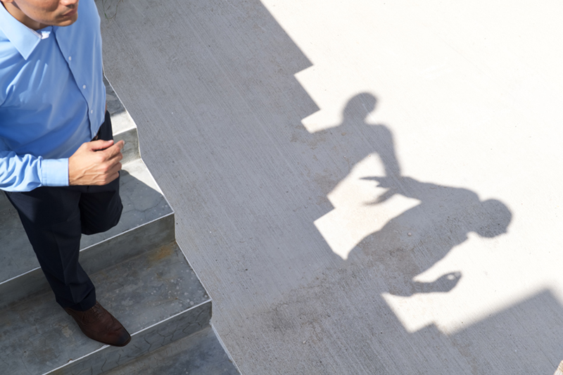 Man in a blue shirt on a staircase, his shadow on the wall beside him